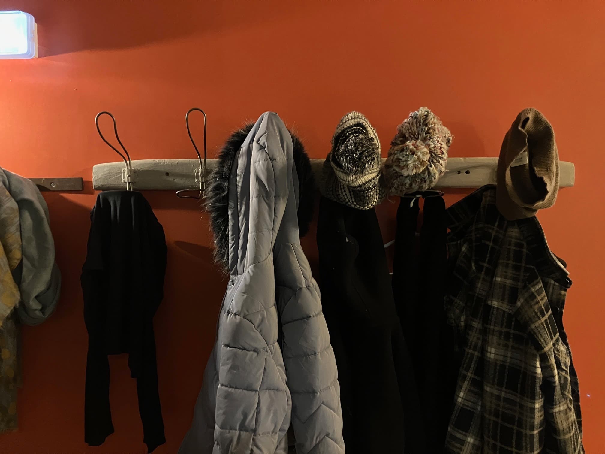 Manteaux et chapeaux accrochés au portemanteau de la Baleine à Bascule, sur un mur orange